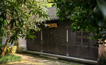 Wooden pavilion entrance at Amanfayun surrounded by lush green foliage.