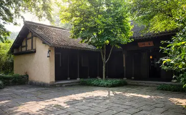 Amanfayun pavilion with thatched roof nestled amongst verdant trees and stone courtyard.