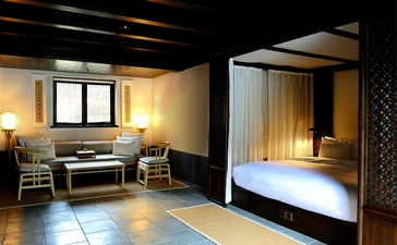Amanfayun suite with wooden ceiling beams, desk area with warm lighting, and separate bedroom alcove with canopied bed.