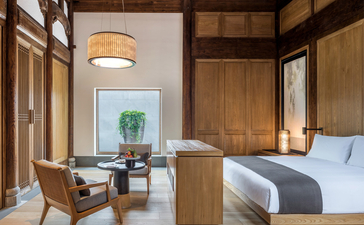 Principal bedroom at Amanyangyun with wooden furnishings, contemporary seating area, and garden views through large windows.