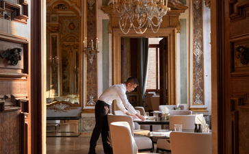 The Ballroom at Aman Venice, with parquet flooring, ornate wooden panelling, crystal chandelier and period furnishings.