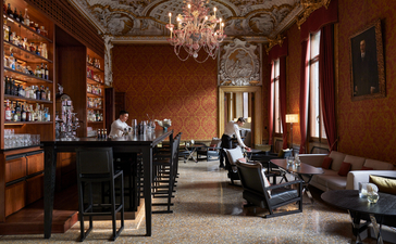 The bar at Aman Venice, with terracotta walls, a crystal chandelier, and vintage furnishings.