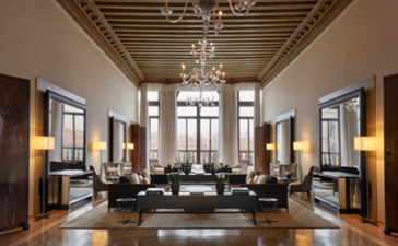 The Drawing Room at Aman Venice, featuring high ceilings, chandeliers, and symmetrical seating arrangements.