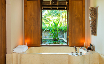 Salle de bains avec baignoire encadrée de bougies et vue sur jardin tropical, Amankila resort, Bali.
