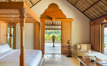 Suite spacieuse à Amankila avec lit à baldaquin en bois, portes ouvertes sur jardin tropical, Bali.