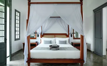Amantaka Pool Suite bedroom with four-poster bed, white linens, and wooden furnishings.