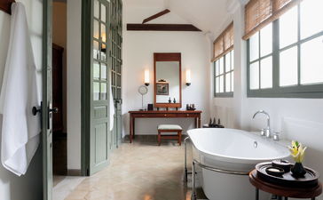 Amantaka Pool Suite bathroom with freestanding bathtub, walk-in shower and garden views through large windows.