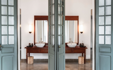Pool Suite bathroom at Amantaka, with twin vanities and large mirrors reflected through glass doors.
