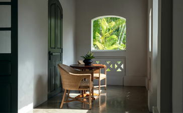 Wooden desk and chair positioned beneath a bright green foliage artwork in a light-filled corridor at Amantaka.