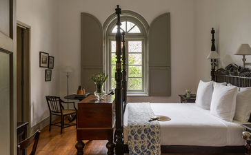 Principal bedroom at Amangalla with arched window and wooden furnishings.