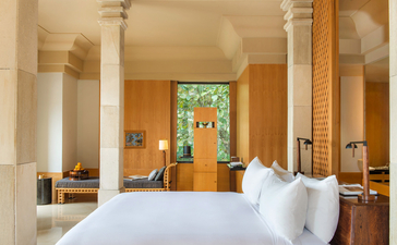 Chambre avec lit blanc et colonnes de pierre au resort Amanjiwo, Indonésie.