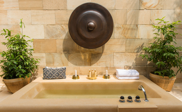 Bassin de la Suite Borobudur à Amanjiwo, avec vasque en pierre, miroir rond et plantes vertes.