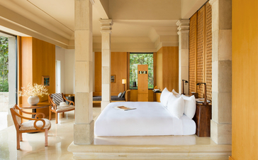 Suite Borobudur avec lit blanc, colonnes et mobilier en bois à Amanjiwo, resort en Indonésie.