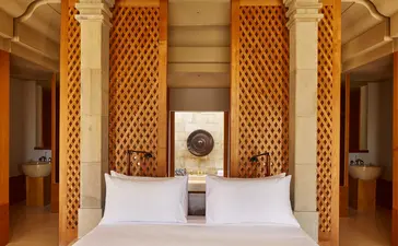 Borobudur Suite bed at Amanjiwo with carved wooden panels and symmetrical doorways.