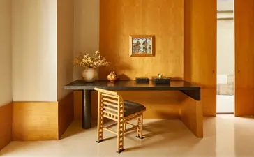 Borobudur Suite workspace at Amanjiwo with wooden desk, woven chair, and warm amber lighting.