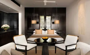 Contemporary Suite at Amansara with wooden dining table, white chairs, and candlelit ambiance.