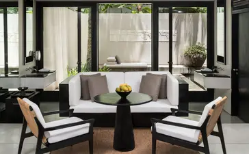 Courtyard Suite seating area at Amansara with curved sofa, round table, and views to gardens beyond.