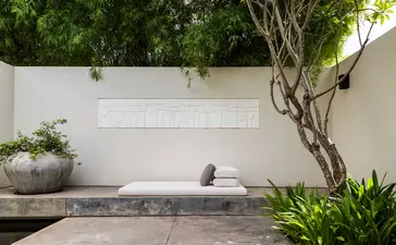 Courtyard at Amansara with white wall, sculptural tree, and stone bench.