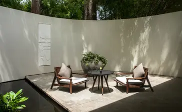 Courtyard at Amansara with two wooden chairs and a round table, dappled sunlight on white walls.