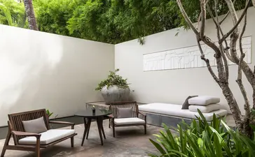 Courtyard seating area at Amansara with wooden chairs, side table, and verdant planting against white walls.