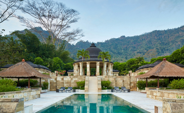Dalem Jiwo Suite at Amanjiwo with reflecting pool and pavilions set against forested hills, Indonesia.