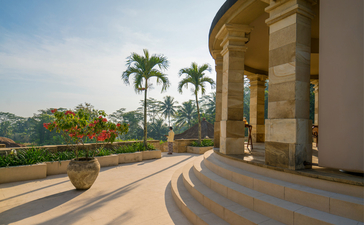 Curved stone terrace with palm trees and distant hills at Amanjiwo, Indonesia.