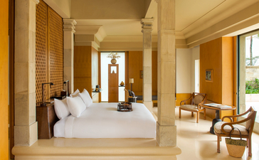 Chambre Garden Suite avec lit principal blanc, portes coulissantes en bois et salon attenant à Amanjiwo Resort, Indonésie.