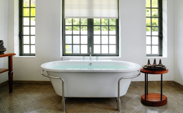 Khan Pool Suite bathroom at Amantaka, with freestanding bathtub and arched windows overlooking Laos.