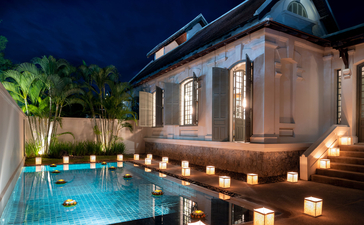 Khan Pool Suite at Amantaka, illuminated at dusk with candlelit poolside and tropical palms.
