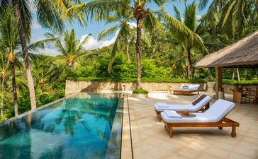 Plunge pool and sun loungers on timber deck at Amankila resort, Bali, surrounded by palm trees.