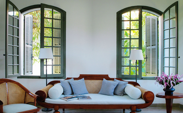 Mekong Pool Suite seating area at Amantaka with curved sofa and arched windows overlooking the Mekong River.