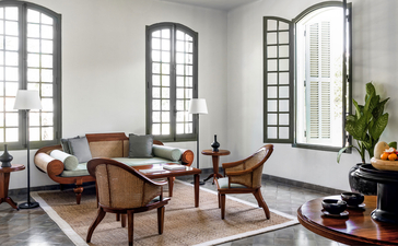 Mekong Pool Suite living area at Amantaka with mid-century furniture and arched windows overlooking Luang Prabang.