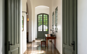 Mekong Pool Suite hallway at Amantaka with green shutters and arched doorway leading to sitting area.