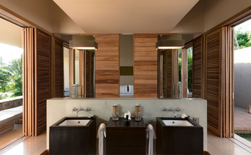 Bathroom at Amanwella with dual vanities, warm wooden panelling, and natural light from large windows.