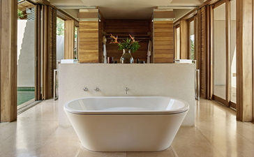 Freestanding oval bath in the Ocean Pool Suite at Amanwella, with wooden cabinetry and glass doors opening to views.