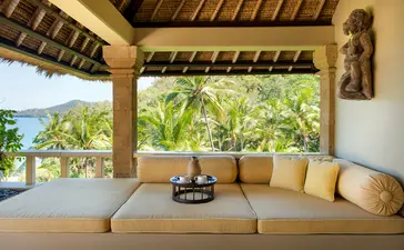 Salon ouvert avec canapé beige et vue sur jardins tropicaux à Amankila, resort à Bali.