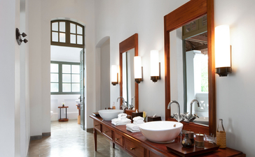 Bathroom at Amantaka with wooden-framed mirror, vintage fixtures, and natural light from window.