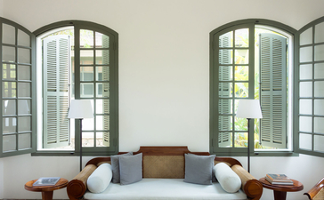 Amantaka suite with arched glass doors opening to views, featuring cushioned seating and warm terracotta vessels.