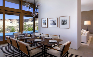 Amangiri dining area with wooden table, chairs, and framed artwork on white walls, overlooking desert landscape through large windows.