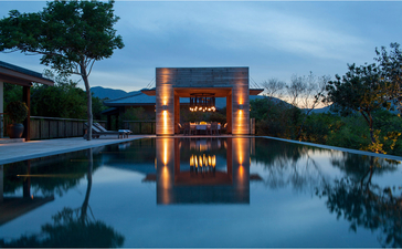 Amanoi リゾートの4ベッドルーム邸宅の照明が灯る建物が静かな水に映る夕暮れの景色。