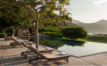 安缦诺怡度假村的五卧室海滨住宅外，木质躺椅面向宁静的水池和远处的山景。