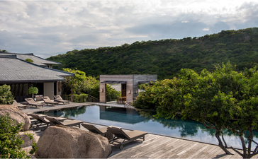 Amanoi resort の5寝室レジデンスの木製デッキから、インフィニティプールと緑豊かな丘陵地を望む。