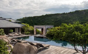 Amanoi resort の5寝室レジデンスの木製デッキから、インフィニティプールと緑豊かな丘陵地を望む。