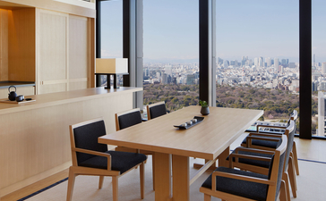 Modern workspace at Aman Tokyo with floor-to-ceiling windows overlooking the city skyline, wooden dining table, and contemporary chairs.