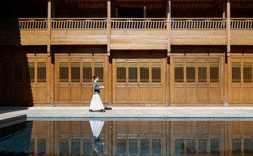 Woman in white seated by plunge pool at Amandayan, reflected in still water with golden wooden structure behind.