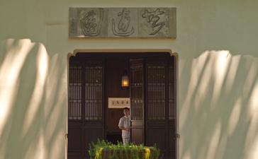 Amanfayun entrance with dark wooden doors framed by white walls and traditional artwork above.