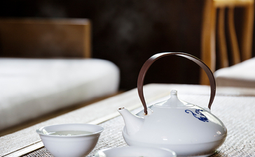Teapot and cups arranged on white cloth at Amanfayun, with wooden chairs in background.