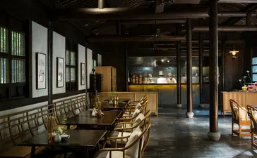 Amanfayun's dining venue with wooden tables and chairs, framed artworks on walls, and warm overhead lighting.
