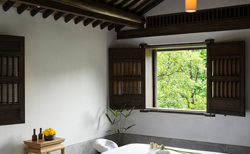 Amanfayun spa treatment room with striped wooden ceiling, pendant lights, and bathtub overlooking garden views.