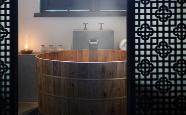 Wooden soaking tub with candlelit ambiance at Amanfayun, framed by geometric screen panels.